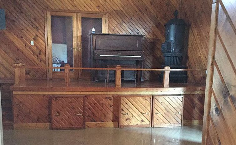 Wood-paneled loft area with an upright piano and wood stove